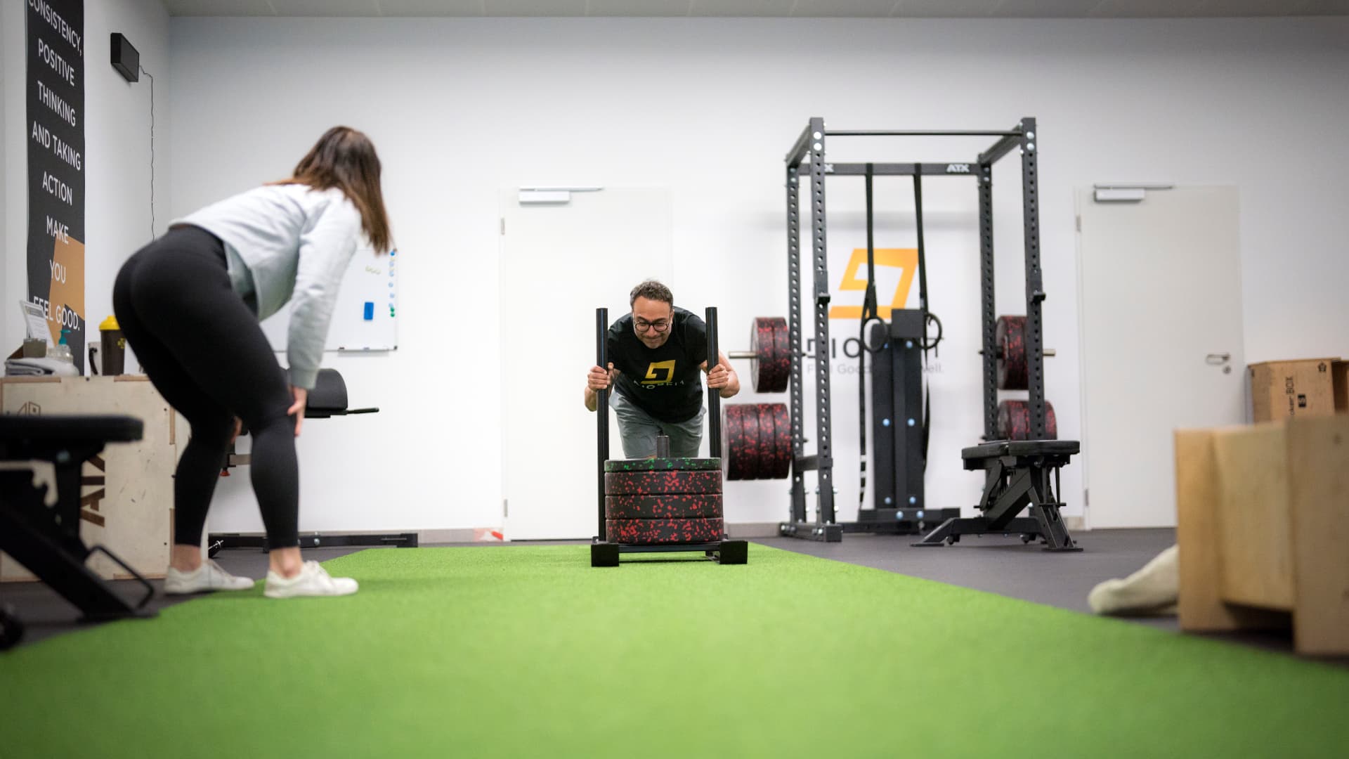 A Diosfit coach pushing an athlete on a weighted sled across the gym turf